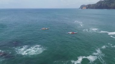 Menganti Beach Kebumen Central Java Endonezya plajının beyaz kum, sakin dalgalar, uçurumlar ve yeşil ağaçlarla insansız hava aracı görüntüsü ve geleneksel balıkçıların ve geleneksel balıkçı teknelerinin faaliyetleri