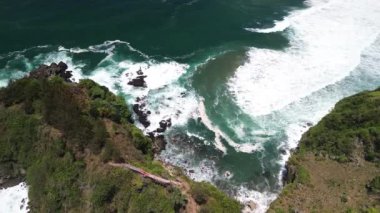 İnsansız hava aracı manzarası Gebyuran Sahili 'ndeki Tanjung Karang Gelini, Kebumen, Merkezi Java, Endonezya, güzel mercan kayalıkları, sakin dalgaları, tepeleri ve yeşil ağaçları olan bir sahil.