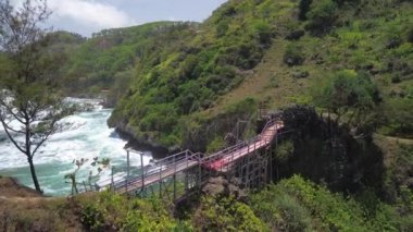 Gebyuran Sahili 'ndeki Tanjung Karang Penganten, Kebumen, Central Java, Endonezya' daki bambu köprüsünün insansız hava aracı görüntüsü, güzel mercan kayalıkları, sakin dalgalar, tepeler ve yeşil ağaçlar.