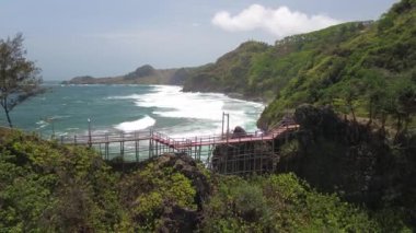 Gebyuran Sahili 'ndeki Tanjung Karang Penganten, Kebumen, Central Java, Endonezya' daki bambu köprüsünün insansız hava aracı görüntüsü, güzel mercan kayalıkları, sakin dalgalar, tepeler ve yeşil ağaçlar.