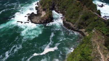 İnsansız hava aracı manzarası Gebyuran Sahili 'ndeki Tanjung Karang Gelini, Kebumen, Merkezi Java, Endonezya, güzel mercan kayalıkları, sakin dalgaları, tepeleri ve yeşil ağaçları olan bir sahil.