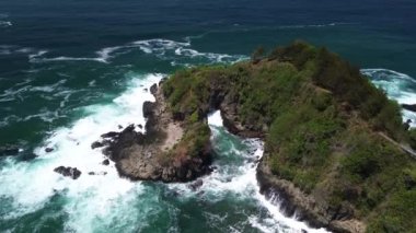 İnsansız hava aracı manzarası Gebyuran Sahili 'ndeki Tanjung Karang Gelini, Kebumen, Merkezi Java, Endonezya, güzel mercan kayalıkları, sakin dalgaları, tepeleri ve yeşil ağaçları olan bir sahil.