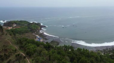 Menganti sahilinin güzelliği, Kebumen, Central Java, Endonezya, sakin deniz dalgaları, mercan kayalıkları ve yeşil ağaçlarla dolu bir sahil.