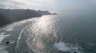 İnsansız hava aracı manzarası Menganti Sahili, Kebumen, Central Java, Endonezya, sakin deniz dalgaları, mercan kayalıkları ve yeşil ağaçlarla dolu bir sahil.