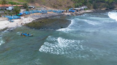 Beyaz kum, sakin dalgalar, uçurumlar ve yeşil ağaçlarla Menganti sahilinin insansız hava aracı görüntüsü ve geleneksel balıkçıların ve balıkçı teknelerinin faaliyetleri