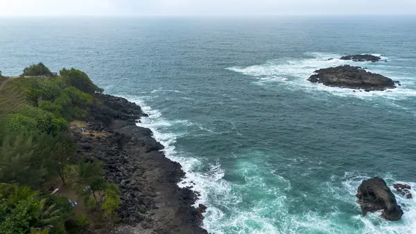 İnsansız hava aracı manzarası Menganti Sahili, Kebumen, Central Java, Endonezya, sakin deniz dalgaları, mercan kayalıkları ve yeşil ağaçlarla dolu bir sahil.