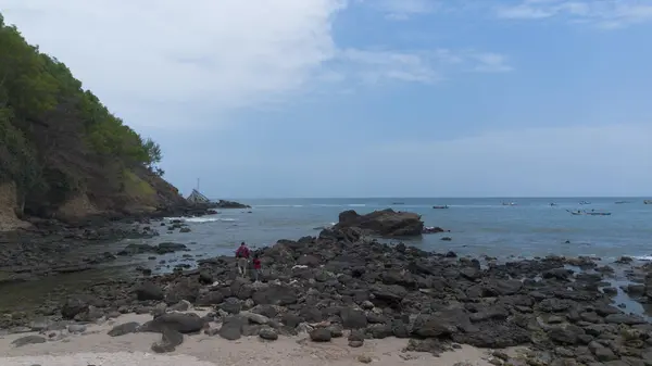 İnsansız hava aracı manzarası Menganti Sahili, Kebumen, Central Java, Endonezya, sakin deniz dalgaları, mercan kayalıkları ve yeşil ağaçlarla dolu bir sahil.