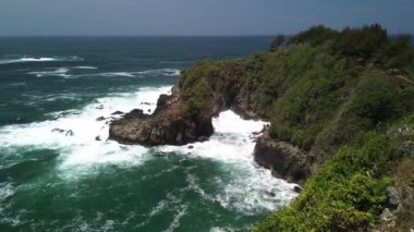 İnsansız hava aracı görüntüsü Gebyuran Sahili 'ndeki Tanjung Karang Penganten güzelliği veya Lampon Sahili, Kebumen, Central Java, Endonezya, güzel mercan kayalıkları, sakin dalgalar, tepeler ve yeşil ağaçlarla dolu bir sahil.