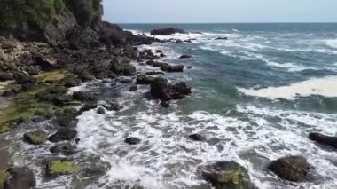 İnsansız hava aracı görüntüsü Gebyuran Sahili 'ndeki Tanjung Karang Penganten güzelliği veya Lampon Sahili, Kebumen, Central Java, Endonezya, güzel mercan kayalıkları, sakin dalgalar, tepeler ve yeşil ağaçlarla dolu bir sahil.