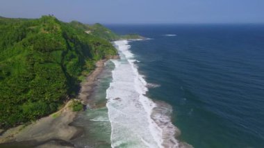 Deniz kenarındaki yeşil tepelerin insansız hava aracı görüntüsü deniz manzaralı dalgalar ve mercan resifleri Pecaron Sahili, Kebumen