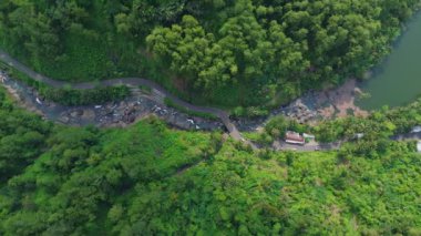 Tepeleri ve yemyeşil ağaçları olan nehir kenarındaki otoyol ve trafiğin en tepedeki drone görüntüsü