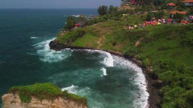 Menganti Sahili 'nin güzelliğinin drone görüntüsü, tepeler, kayalar ve dalgalarla çevrili deniz kenarlı Kebumen ve kamp için bir yer.