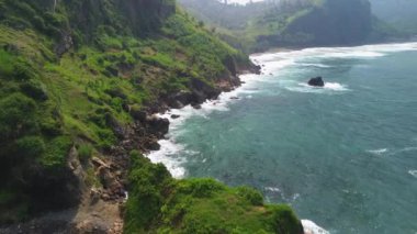Menganti sahilinin insansız hava aracı görüntüsü tepeleri ve dalgalar ve kayalarla çevrili yeşil ağaçları olan Kebumen.