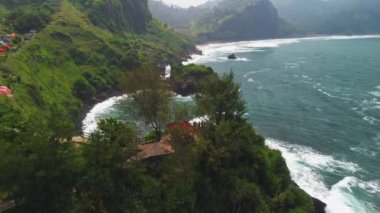 Menganti Sahili 'nin güzelliğinin drone görüntüsü, deniz manzaralı Kebumen tepeler, kayalar ve dalgalarla çevrili.