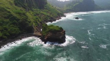 Menganti Sahili 'nin güzelliğinin drone görüntüsü, deniz manzaralı Kebumen tepeler, kayalar ve dalgalarla çevrili.