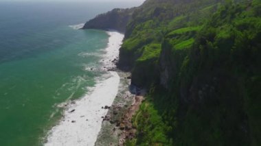 Uçurumlar, verimli tepeler, okyanustan gelen dalgalar ve Endonezya 'nın etrafındaki ağaçlarla dolu deniz manzarası.