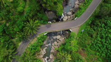 Tepeler, ormanlar ve yanında bir nehir akan yeşil ağaçların ortasındaki trafik ve otoyolların drone görüntüsü.