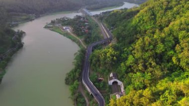 Serayu Nehri Barajı 'nın hava aracı görüntüsü. Arkasında tepeler ve ağaçlar olan yollar, trafik ve demiryolları var.