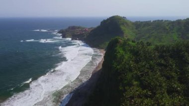 Deniz kıyısının insansız hava aracı görüntüsü yemyeşil tepeler ve ağaçlarla mercan kayalıkları ve denizden gelen dalgalar Pecaron Sahili kebumen Endonezya 'da