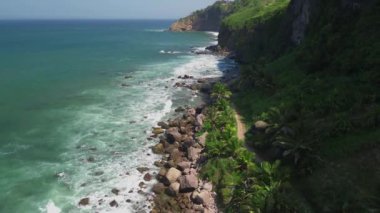 Deniz kıyısındaki insansız hava aracı manzarası yemyeşil tepeler ve mercan kayalıkları ve okyanustan gelen dalgalarla dolu ağaçlarla dolu.