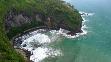 Drone view of Jerit hill Kebumen Indonesia, the seaside with beautiful hills and green trees, coral rocks, waves and ocean clipart