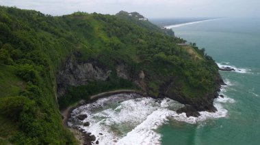 Jerit Hill Kebumen Endonezya 'nın insansız hava aracı manzarası, güzel tepeleri, yeşil ağaçları, mercan kayaları, dalgaları ve okyanusları olan deniz kıyısı.