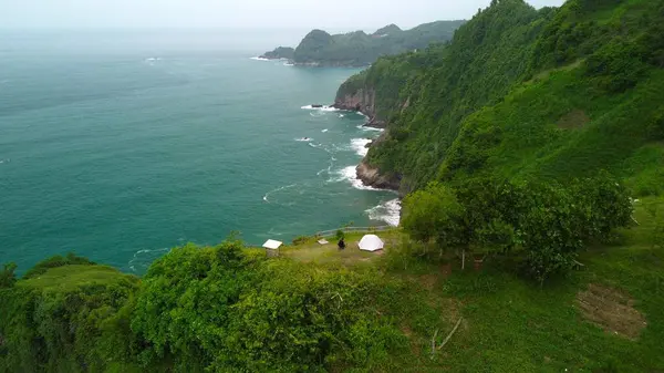 Hava görüntülü insansız hava aracı kamerası 4k. Bir adam sahilde ve kıyılarda kamp yapıyor. Jerit Hill Kebumen merkez java Endonezya 'da güzel dalgalarla çevrili.