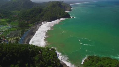 Kumsalları, tepeleri, ağaçları ve geleneksel balıkçı tekneleri kenetlenmiş kıyı şeridi manzarası.