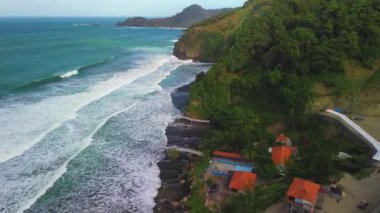 Hava aracı Endonezya 'nın Surumanis Sahili Kebumen bölgesindeki tepeler, yeşil ağaçlar, mercanlar ve okyanustan gelen dalgalarla kıyı şeridine bakıyor.