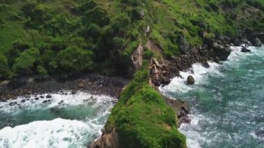 Menganti Beach Kebumen Central Java Endonezya 'daki tepeler, yeşil ağaçlar, mercanlar ve okyanustan gelen dalgalarla hava aracı kıyı şeridi görüntüsü.