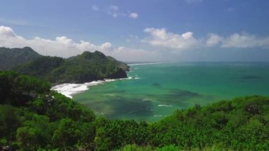 Aerial drone view of a man standing on the coastline with hills and green trees, coral and waves from the sea at Surumanis Beach Kebumen Indonesia