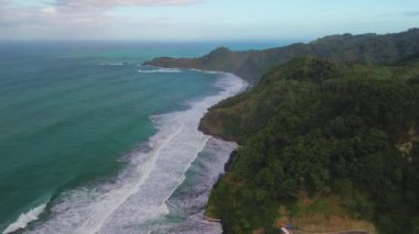 Kıyı şeridinin güzelliğinin hava aracı görüntüsü tepeler ve yeşil ağaçlarla mercan, sahil kumu ve deniz dalgaları Surumanis plajı Kebumen Central Java Endonezya 'dan