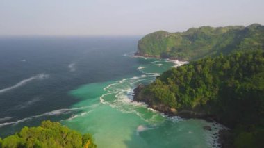 Sawangan plajı Kebumen Central Java Endonezya 'daki tepeler, yeşil ağaçlar, mercan, sahil kumu ve okyanus dalgalarıyla kıyı şeridinin güzelliğini gösteren hava aracı görüntüsü.