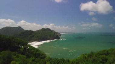 Kıyı şeridinin güzelliğinin hava aracı görüntüsü tepeler, mercan, kumsal ve okyanustan gelen dalgalarla yeşil ağaçlar.
