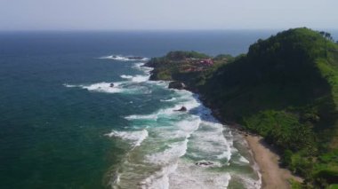 İnsansız hava aracı Pecaron plajı Kebumen Central Java Endonezya 'daki tepeler, ağaçlar, mercanlar ve denizden gelen dalgalarla kıyı şeridini görüyor.