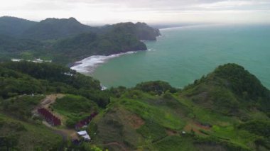 Tepeleri ve ağaçları olan kıyı şeridinin hava aracı görüntüsü, aynı zamanda mercan kayalıkları ve deniz manzarası Surumanis Plajı Kebumen Central Java Endonezya 'dan dalga dalga geliyor.