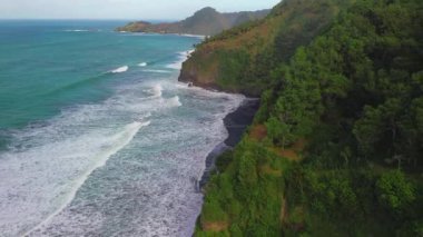 Tepeleri ve ağaçları olan kıyı şeridinin hava aracı görüntüsü, aynı zamanda mercan kayalıkları ve deniz manzarası Surumanis Plajı Kebumen Central Java Endonezya 'dan dalga dalga geliyor.