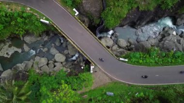 Tepelerin, ormanların ve ağaçların arasında kayaların ve akan suların olduğu bir nehri geçen karayolu ve trafik manzarasının en aşağısında.