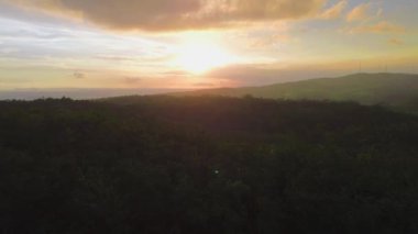 İnsansız hava aracı ağaçların ve ormanların üzerinden uçuyor. Günbatımı ve tepeler öğleden sonraya kadar arka planda kalıyor.