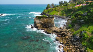 Tepeleri ve ağaçları olan kıyı şeridinin hava aracı görüntüsü, aynı zamanda mercan kayalıkları ve okyanus manzarası Menganti Beach Kebumen Central Java Endonezya 'da.