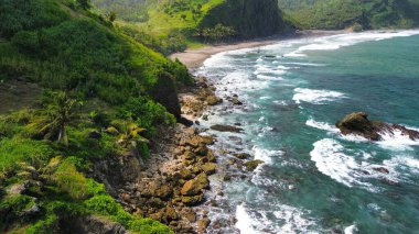 Tepeleri ve ağaçları olan kıyı şeridinin hava aracı görüntüsü, aynı zamanda mercan kayalıkları ve okyanus manzarası Menganti Beach Kebumen Central Java Endonezya 'da.