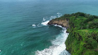 Tepeler ve ağaçlarla dolu kıyı şeridinin hava aracı görüntüsü, aynı zamanda mercan kayalıkları ve deniz manzarası Menganti Beach Kebumen Central Java Endonezya 'dan dalga dalga geliyor.