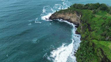 Tepeler ve ağaçlarla dolu kıyı şeridinin hava aracı görüntüsü, aynı zamanda mercan kayalıkları ve deniz manzarası Menganti Beach Kebumen Central Java Endonezya 'dan dalga dalga geliyor.