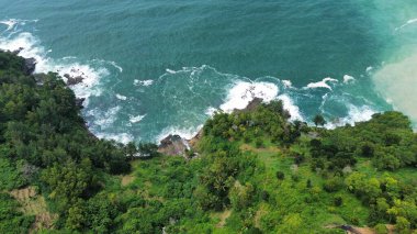 Tepeler ve ağaçlarla dolu kıyı şeridinin hava aracı görüntüsü, aynı zamanda mercan kayalıkları ve deniz manzarası Menganti Beach Kebumen Central Java Endonezya 'dan dalga dalga geliyor.