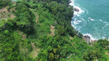 Tepeler ve ağaçlarla dolu kıyı şeridinin hava aracı görüntüsü, aynı zamanda mercan kayalıkları ve deniz manzarası Menganti Beach Kebumen Central Java Endonezya 'dan dalga dalga geliyor.