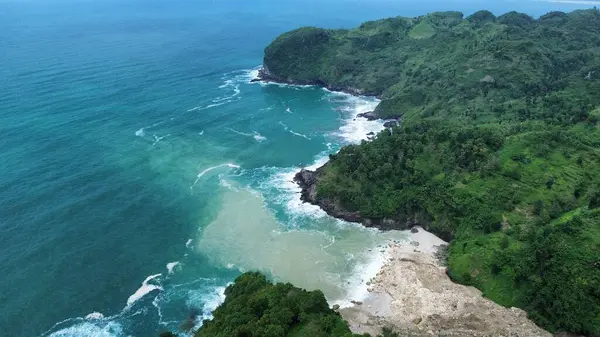 Tepeler ve ağaçlarla dolu kıyı şeridinin hava aracı görüntüsü, aynı zamanda mercan kayalıkları ve deniz manzarası Menganti Beach Kebumen Central Java Endonezya 'dan dalga dalga geliyor.