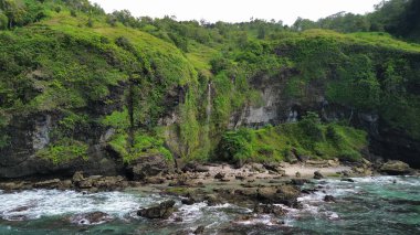 Tepeleri ve ağaçları olan kıyı şeridinin hava aracı görüntüsü, aynı zamanda mercan kayalıkları ve okyanus manzarası Menganti Beach Kebumen Central Java Endonezya 'da.