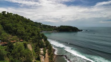 Tepeleri ve ağaçları olan kıyı şeridinin hava aracı görüntüsü, aynı zamanda mercan kayalıkları ve okyanus manzarası Menganti Beach Kebumen Central Java Endonezya 'da.