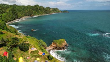 Tepeleri ve ağaçları olan kıyı şeridinin hava aracı görüntüsü, aynı zamanda mercan kayalıkları ve okyanus manzarası Menganti Beach Kebumen Central Java Endonezya 'da.