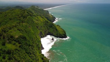 Tepeler ve ağaçlarla kıyı şeridini gösteren hava aracı manzarası, Watu Bale Beach Kebumen Central Java Endonezya 'daki mercan kayalıkları ve deniz dalgaları.